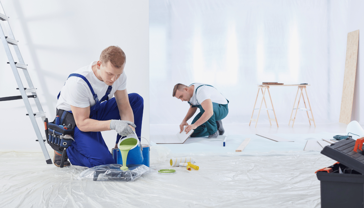 Two men are painting a wall in a room.