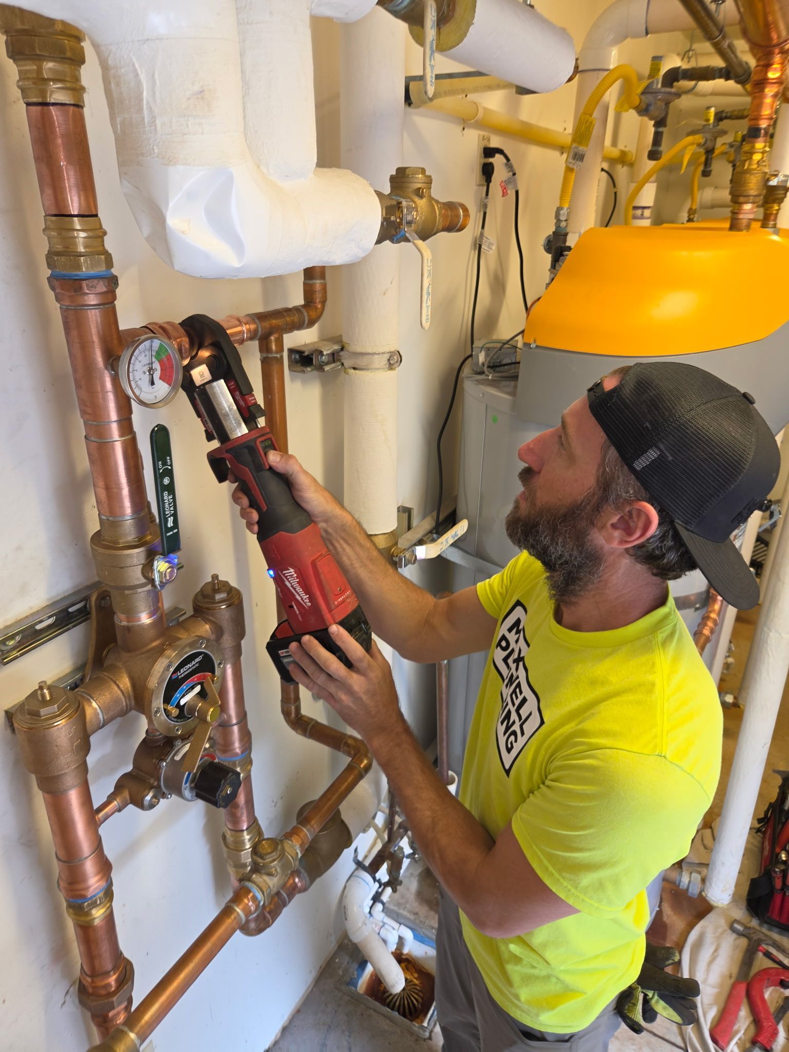 Worker using a red power tool to inspect pipes and valves in a mechanical room