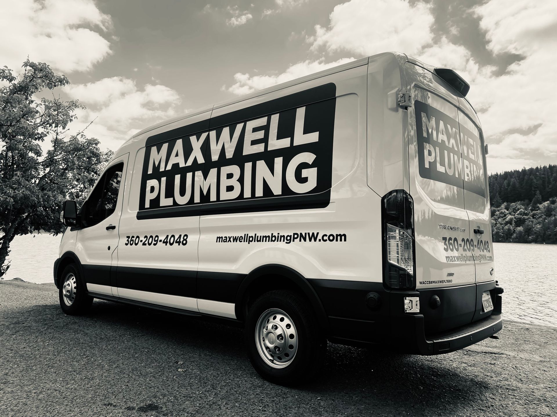 White MAXWELL PLUMBING van parked outdoors on a gravel lot under cloudy skies
