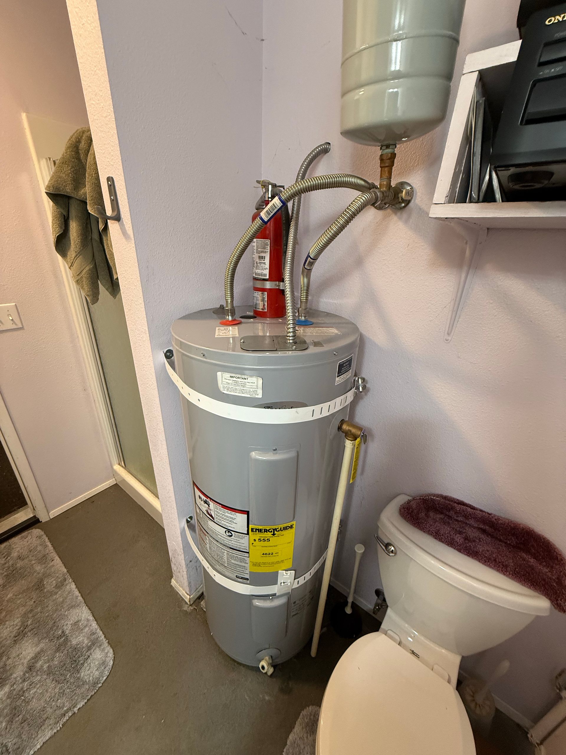 Water heater in a corner next to a toilet; a bathroom.