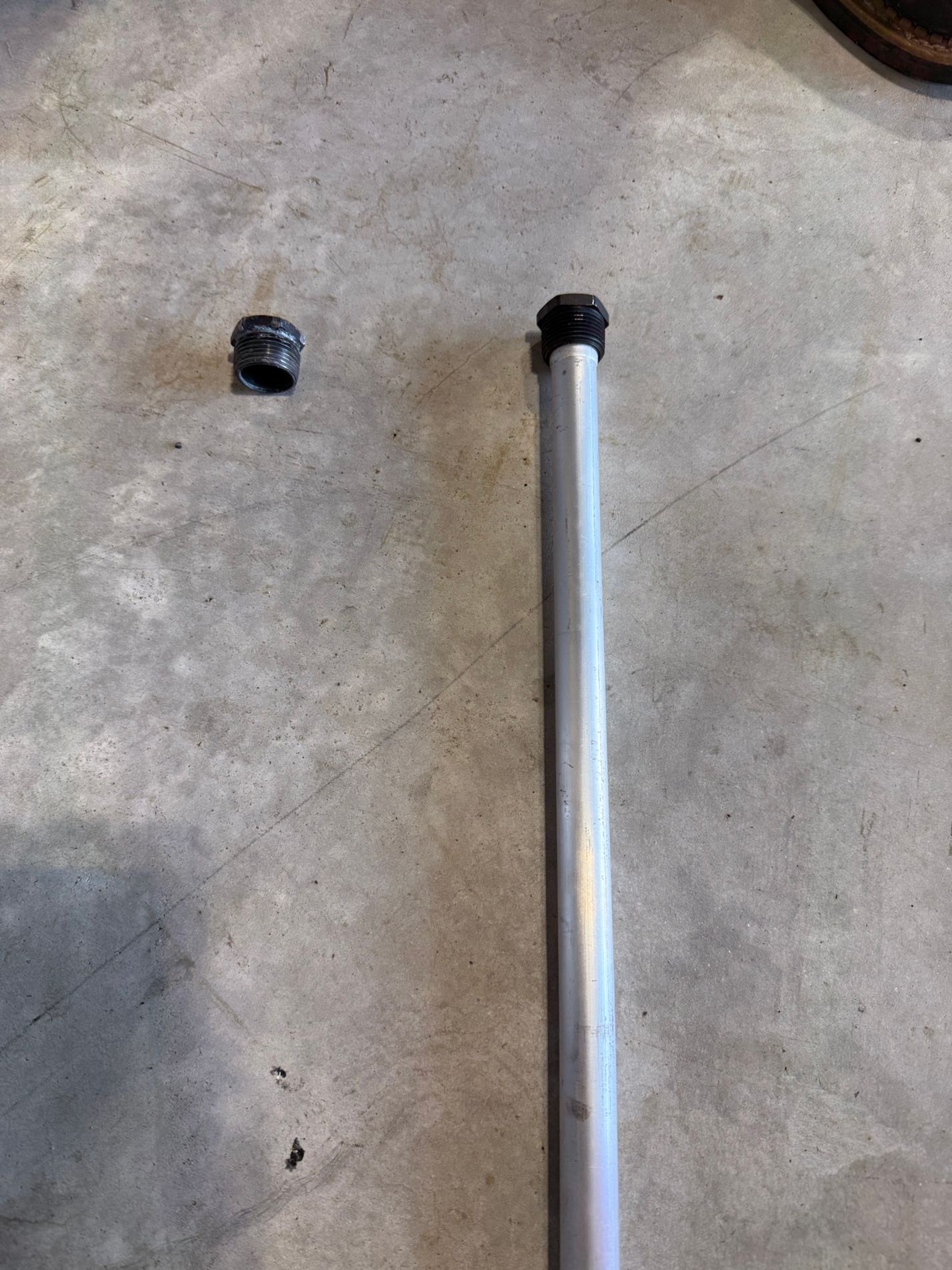 A metal pole with rubber stoppers on a concrete surface. One stopper is detached.