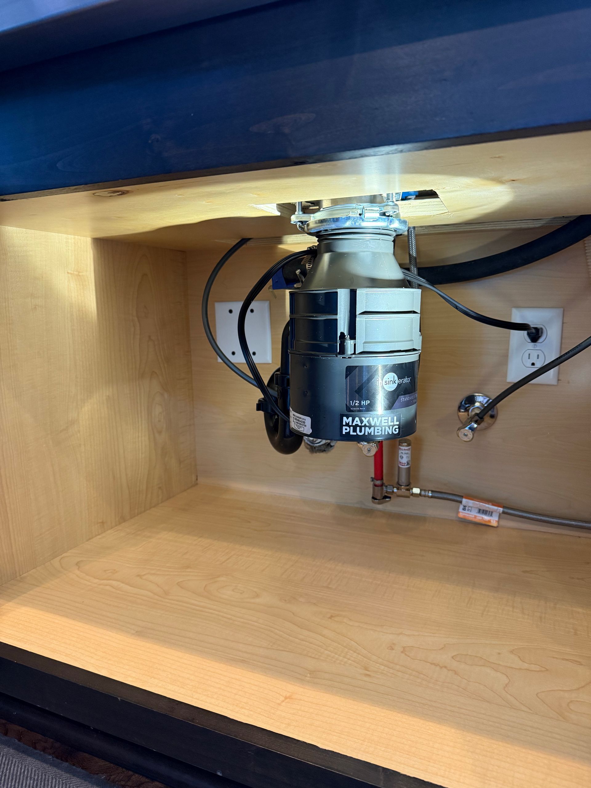 Garbage disposal unit installed under a kitchen sink. Plumbing and electrical connections visible.