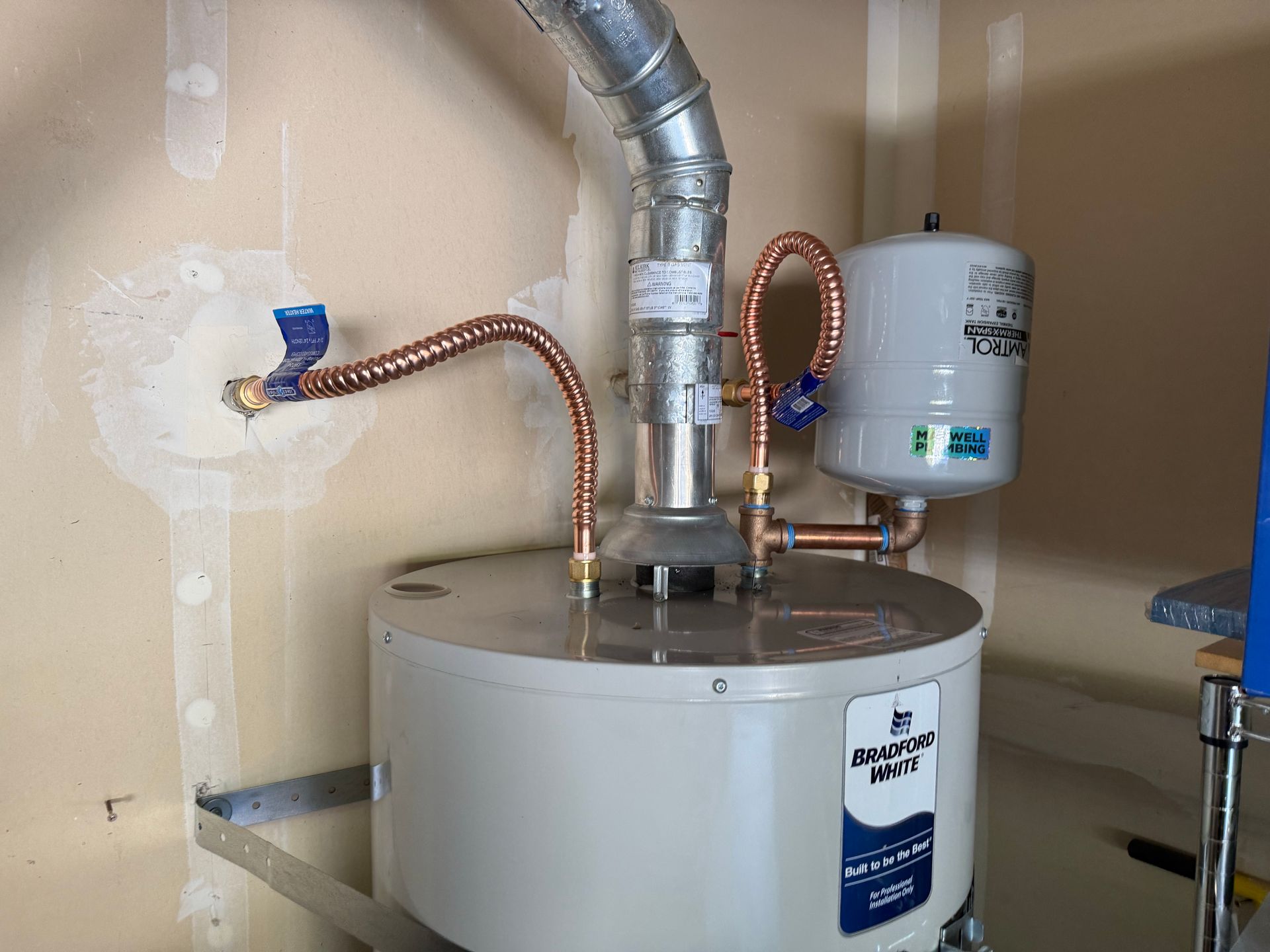 Water heater installation with copper pipes and expansion tank in a garage.