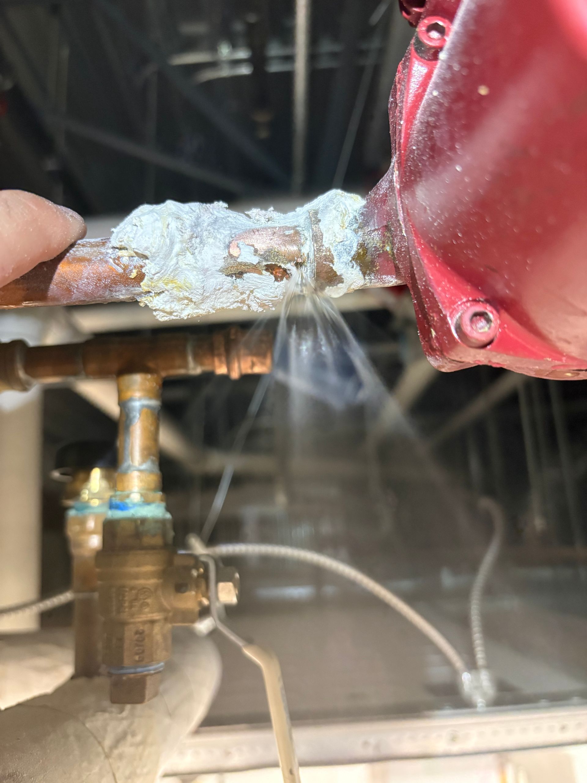 Water spraying from a corroded pipe next to a red machine component