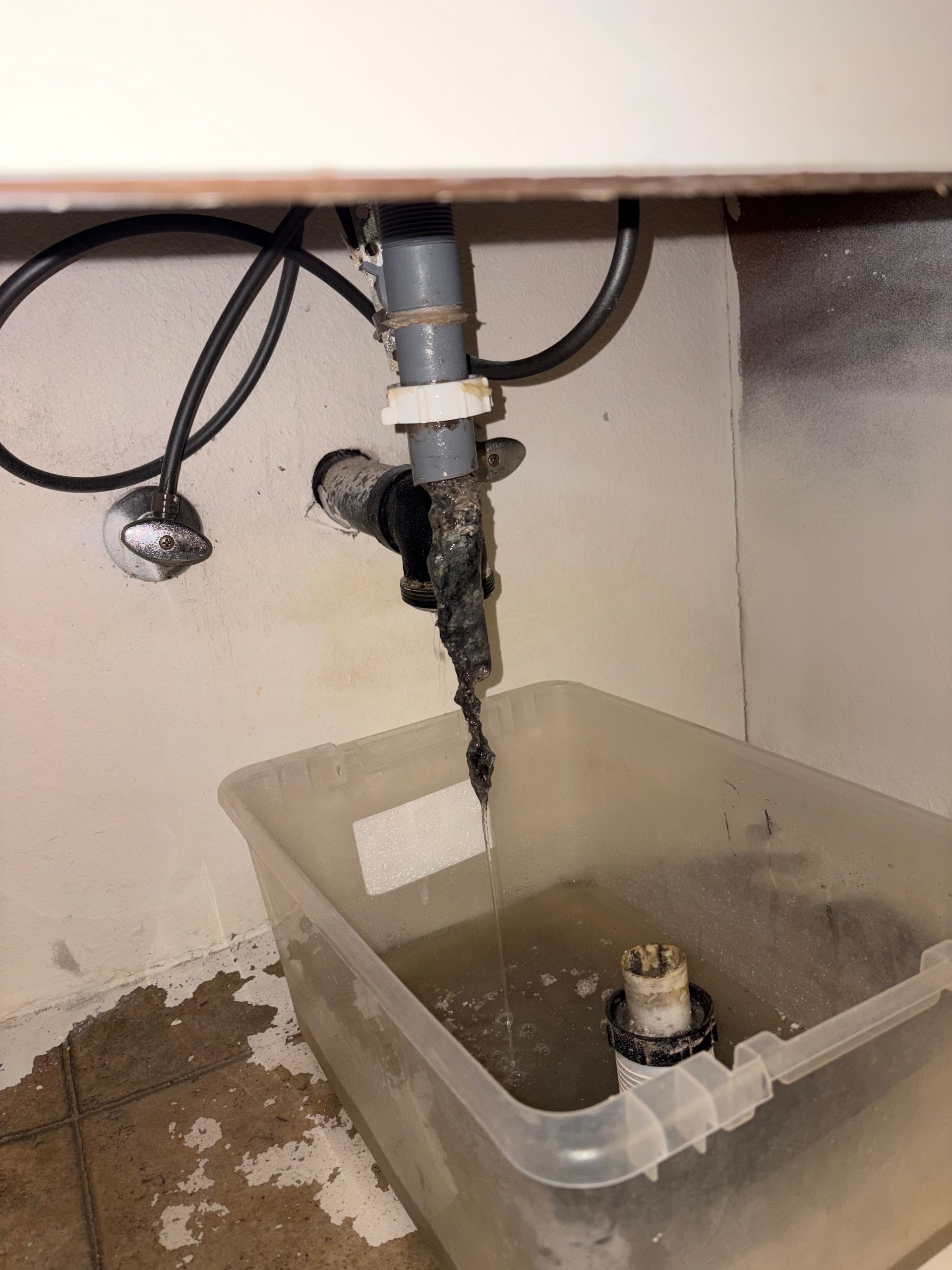 Leaking sink drain with water dripping into a clear plastic bin under the cabinet