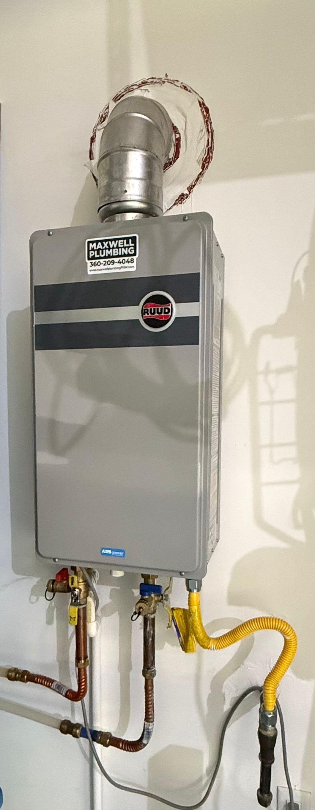 A wall-mounted, tankless water heater with vent pipe and connected plumbing.