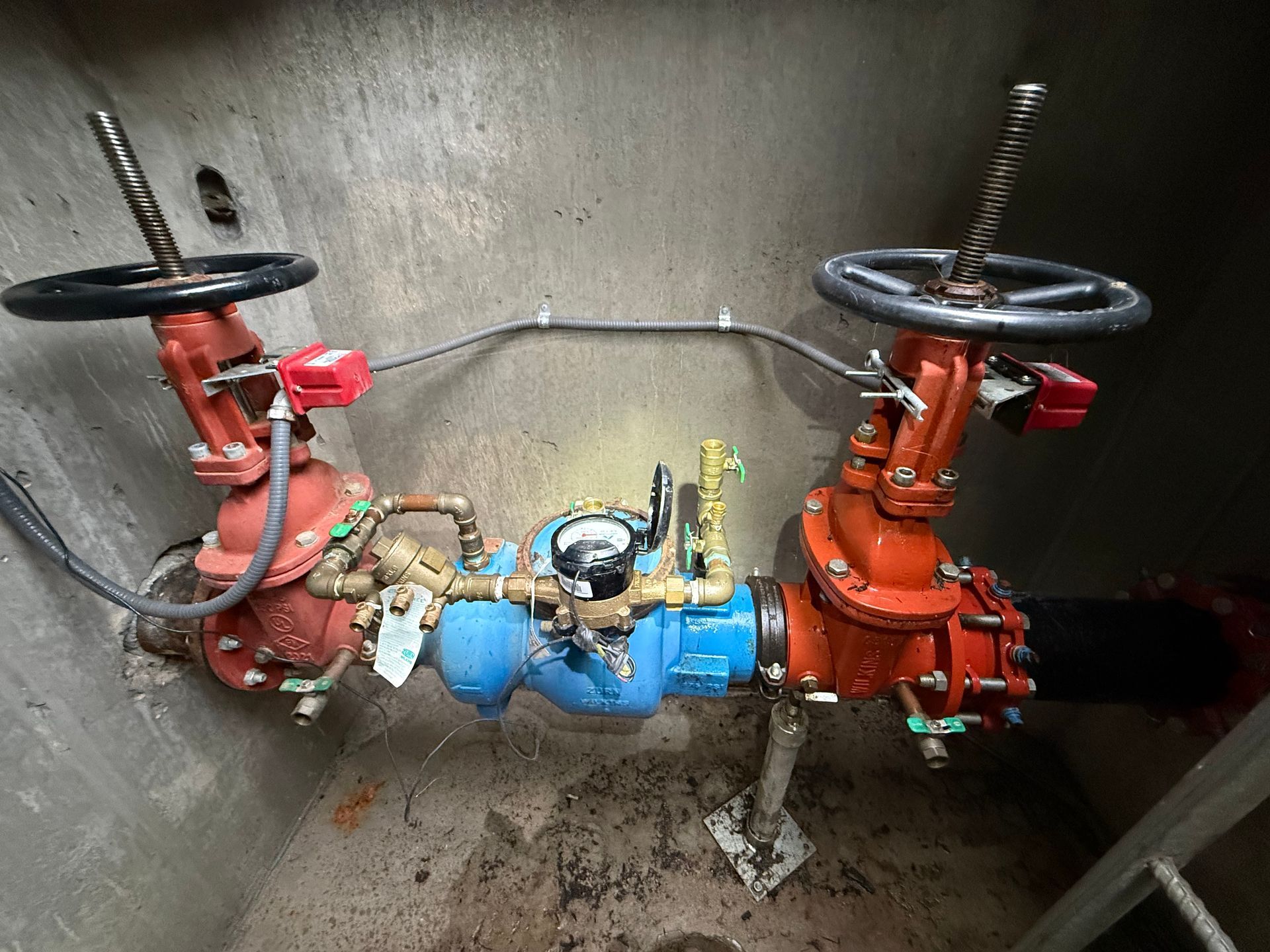 Industrial valve assembly with red and blue pipes and handwheel valves inside a metal enclosure