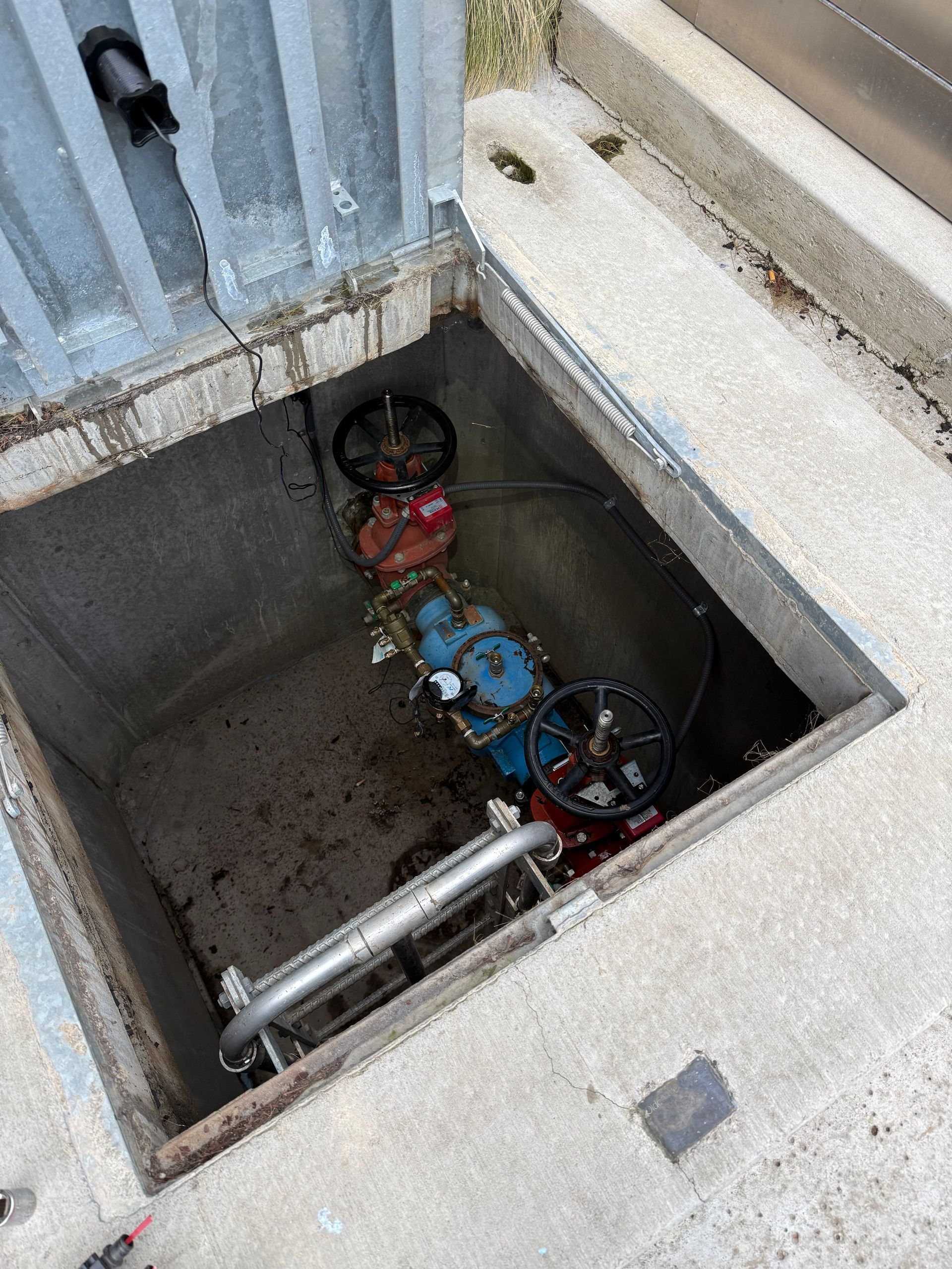 Open utility pit with water meters, pipes, and valves inside a concrete enclosure