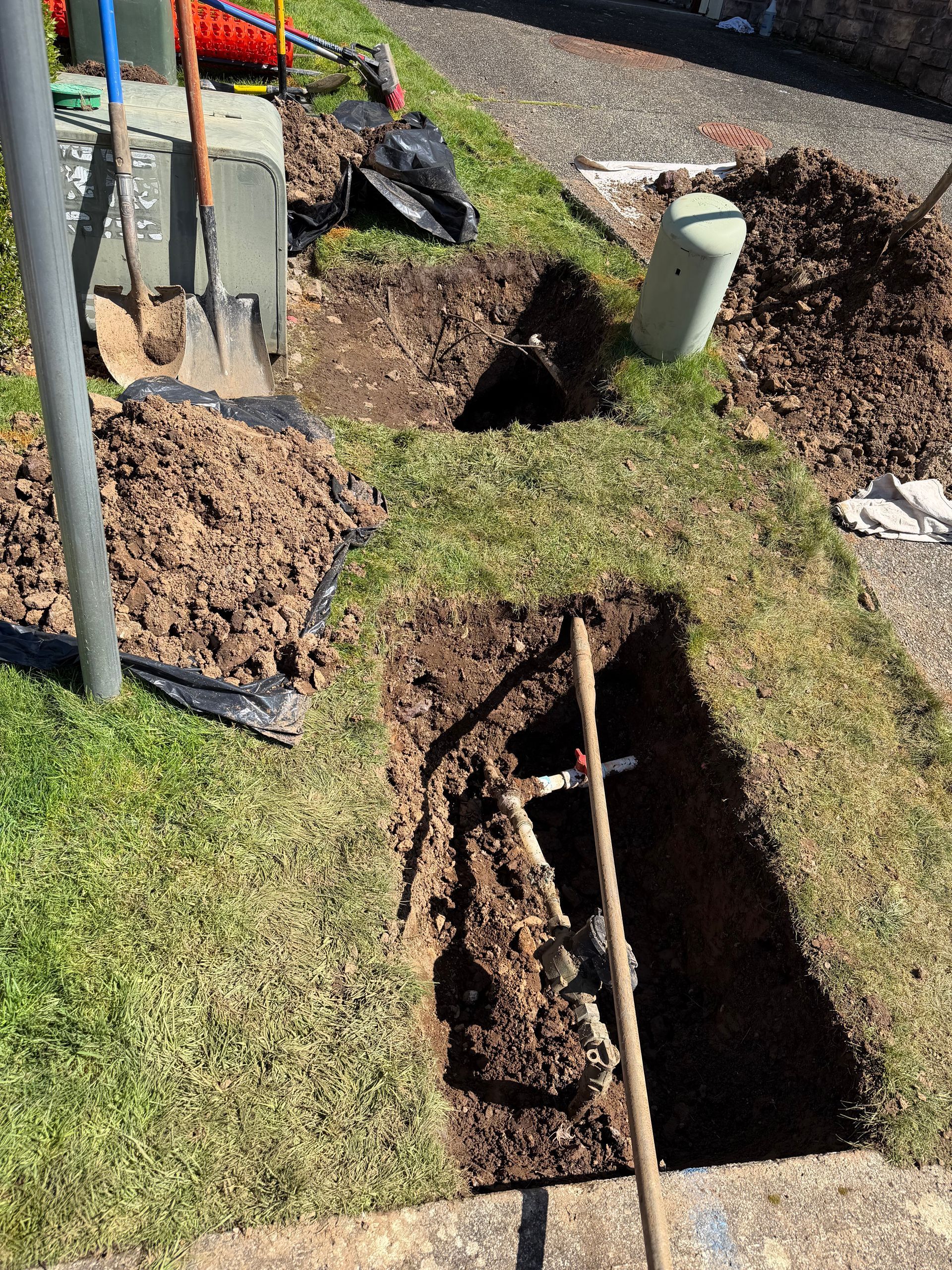 Open trenches and utility pipes in a grassy yard during construction work