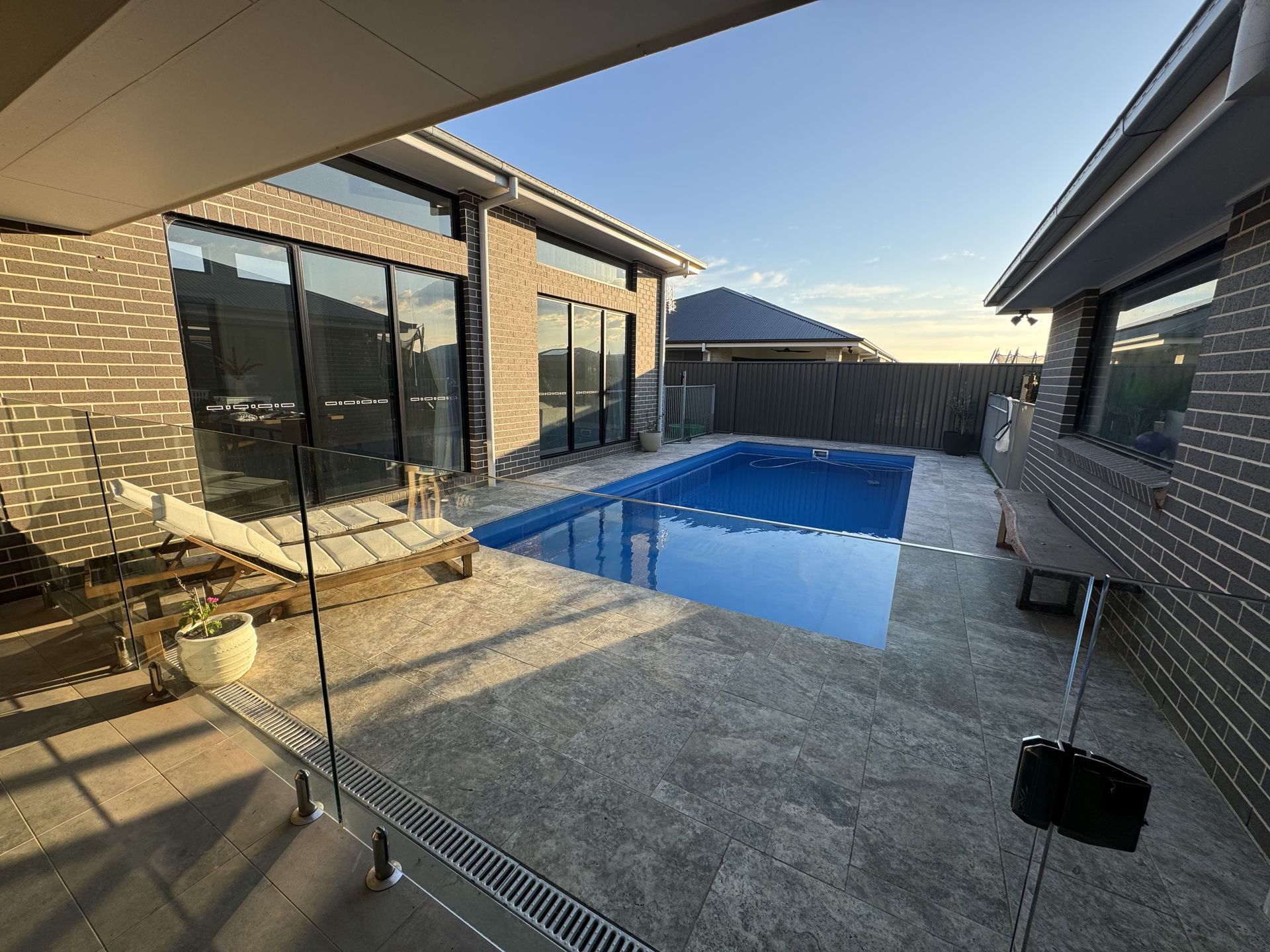 Backyard with a pool between two brick buildings. Concrete patio, blue pool water, sunny day.