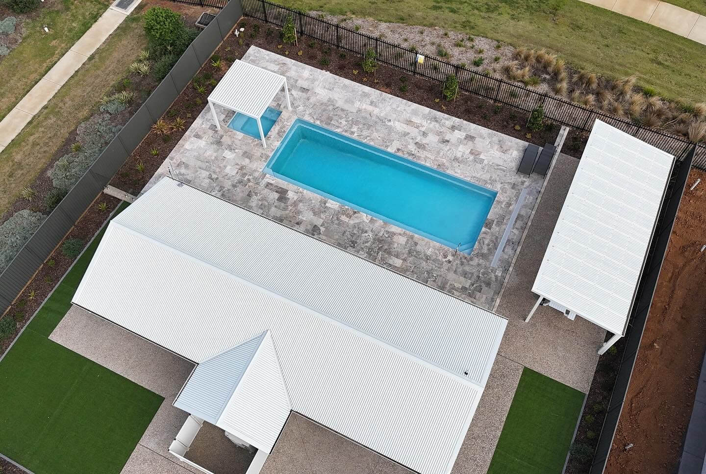 Aerial view: white house with pool and carport; turquoise water, light stone patio.