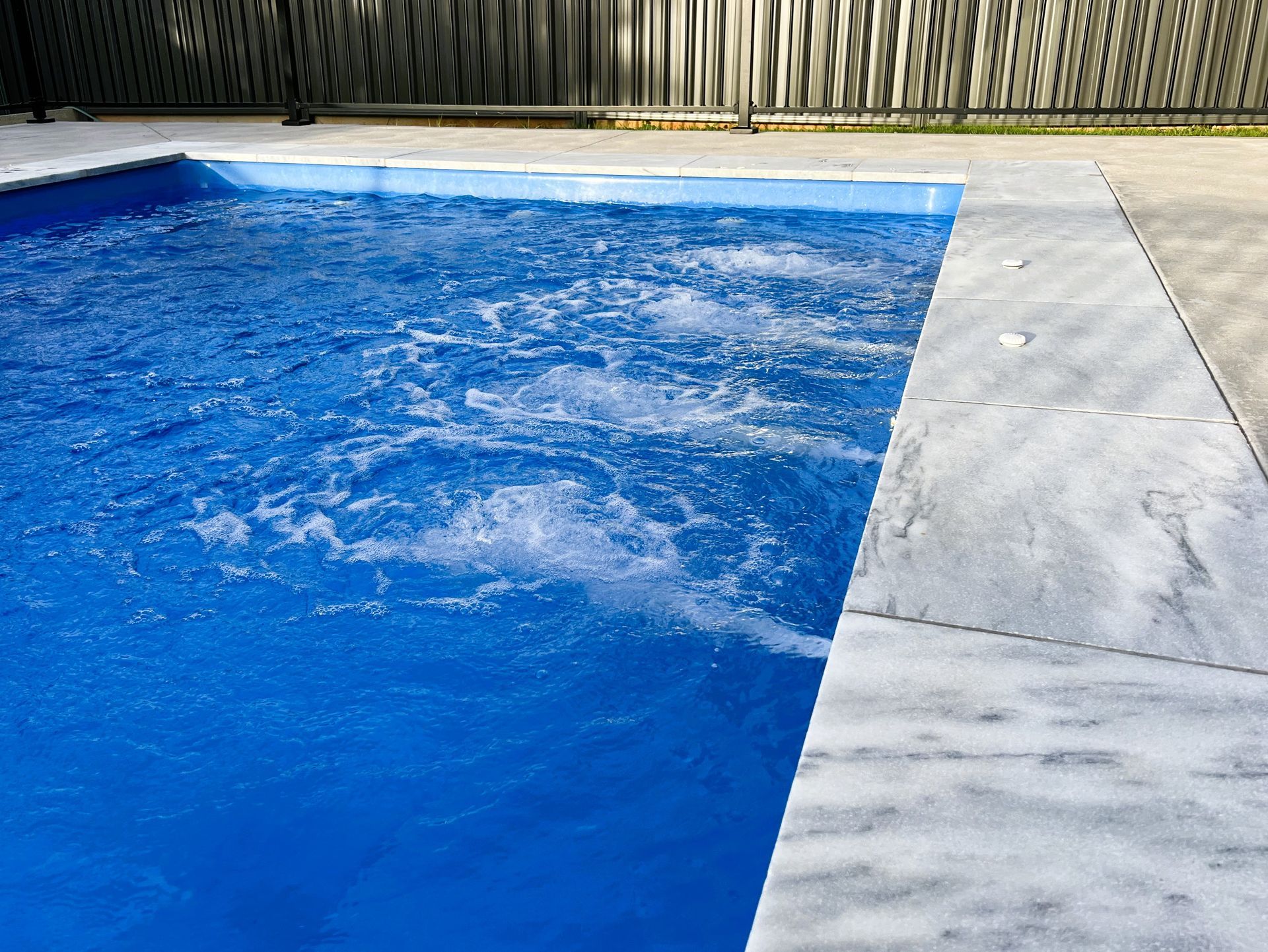 A blue swimming pool with bubbling water next to a gray concrete deck.