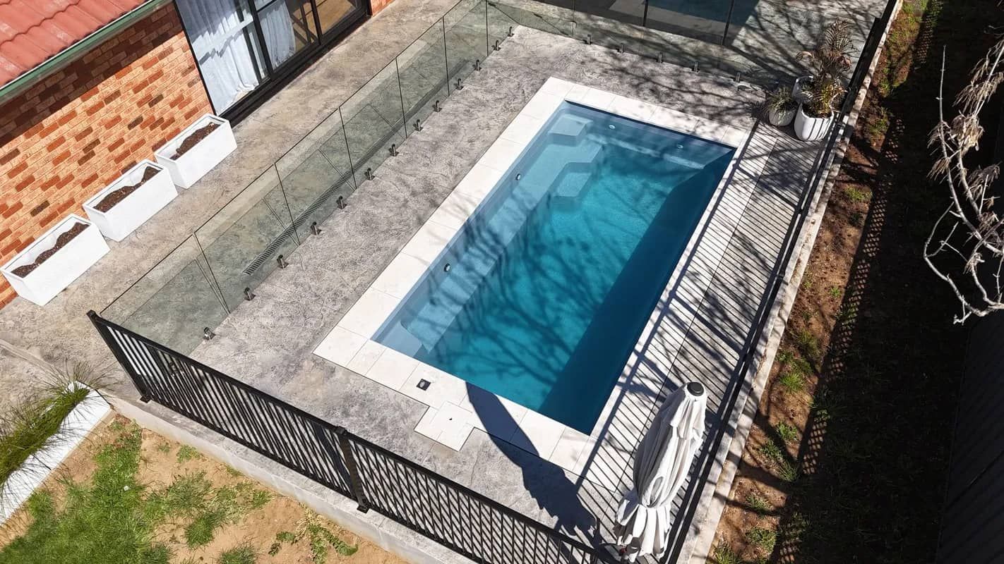 Rectangular outdoor pool with blue water, concrete surround, and black fencing.
