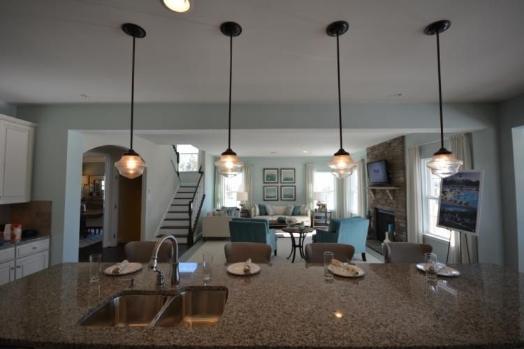 Kitchen with pendant lights above an island, overlooking a living area with furniture and fireplace.