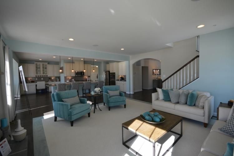 Spacious living room with blue accent walls, aqua chairs, white sofa, and open kitchen.