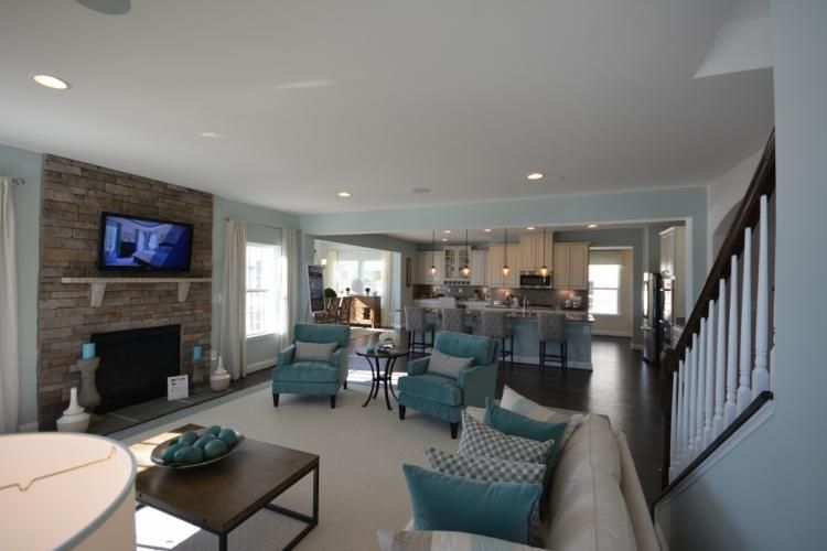 Living room with fireplace, open to kitchen; teal accents, light blue walls, dark hardwood floors.