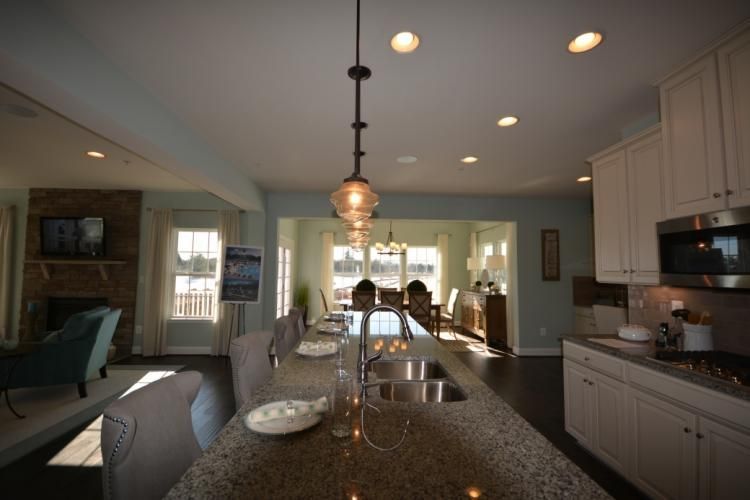 Kitchen with island, dining area, and living room visible. Light blue walls, white cabinets, dark countertops.