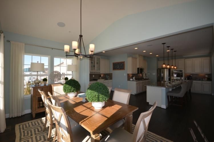 Dining room with table and chairs, open to kitchen; light blue walls, dark wood floor.
