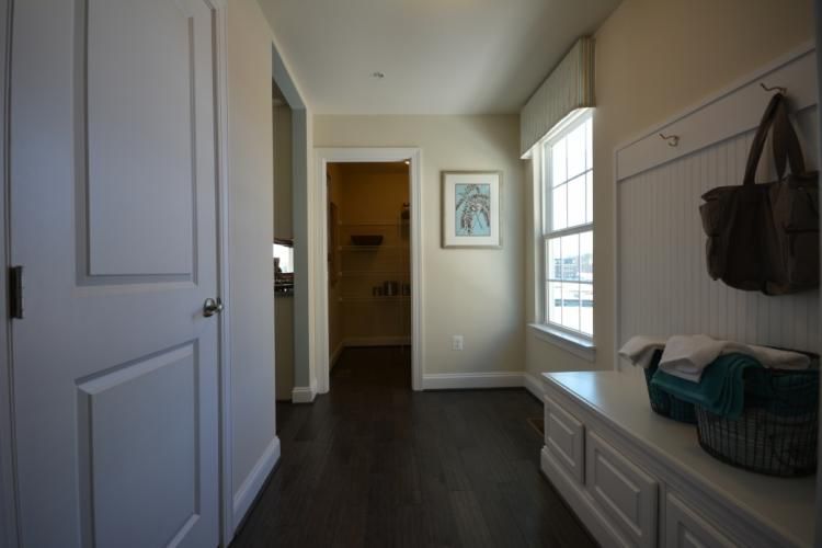 Hallway with dark wood floor, white door, and built-in bench. Laundry room visible down the hall.