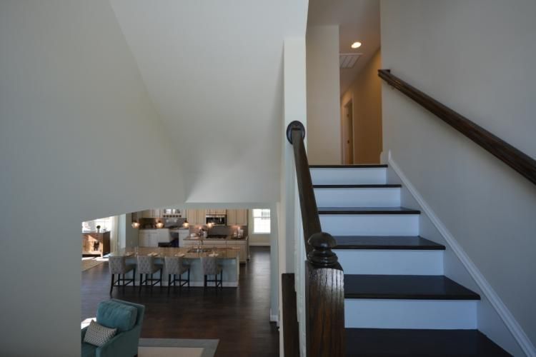 Interior view of a staircase leading upstairs, with white walls, dark wood stairs, and a view into a kitchen.