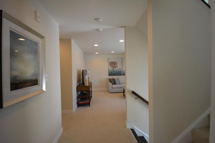 Hallway with carpet leads to a sitting area. Artwork on walls. TV on a stand. Neutral colors.