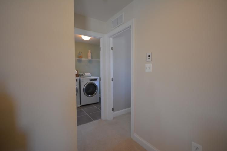 Hallway with a laundry room and closed door. Beige walls, washer, dryer, and shelves are visible.