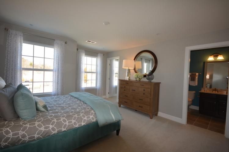 Bedroom with bed, dresser, windows, and doorway to a bathroom; light blue and neutral colors.