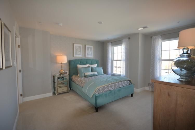 Bedroom with blue bed, nightstand, dresser, two windows, neutral walls and carpet.