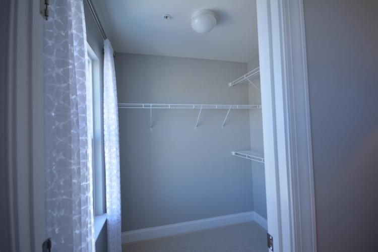 Empty closet with white wire shelving, window with sheer curtains. Pale gray walls and door frame.
