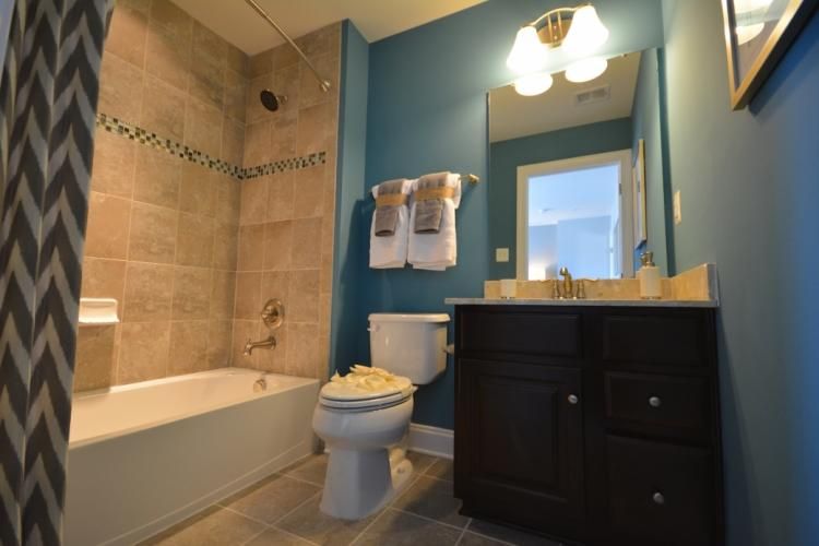 Bathroom with beige tiled shower, blue walls, dark vanity, white toilet, and gray patterned shower curtain.