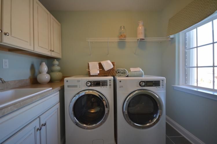 Laundry room with white washer and dryer, cabinets, sink, and window with shade.