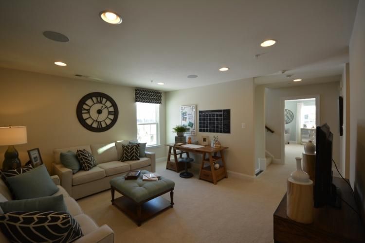 Living room with two sofas, a desk, a clock, and a window. Beige walls and carpet, neutral tones.