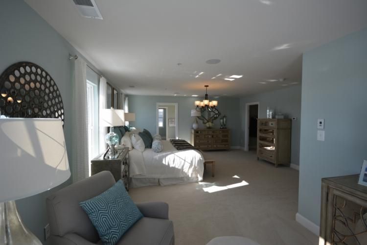 Spacious bedroom with light blue walls, soft carpet, and natural light. Includes bed, chair, and dresser.