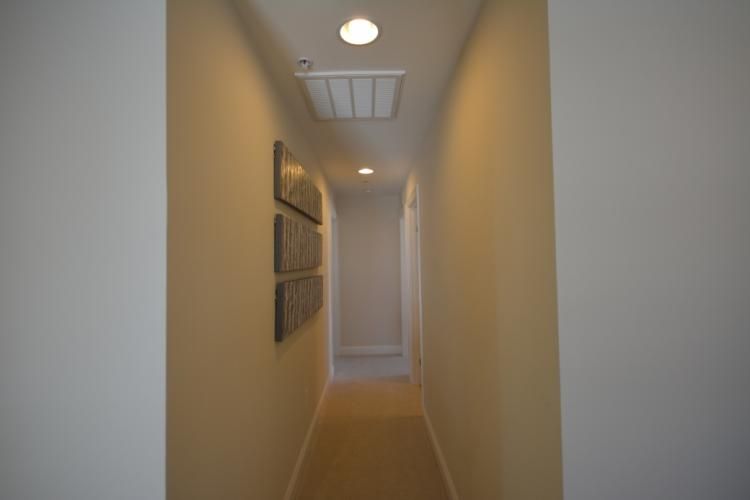 Narrow hallway with beige walls, recessed lights, and art.
