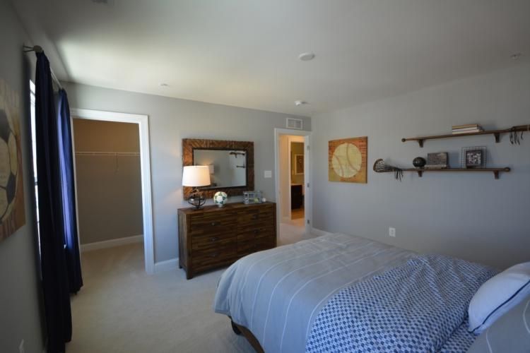 Bedroom with gray walls, bed with blue bedding, wooden dresser with mirror, and open closet.