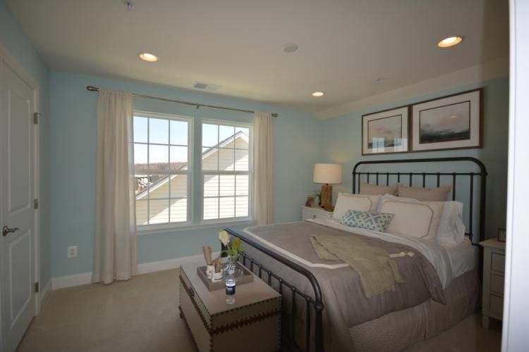 Bedroom with light blue walls, window, wrought iron bed, artwork, and neutral-toned furniture.