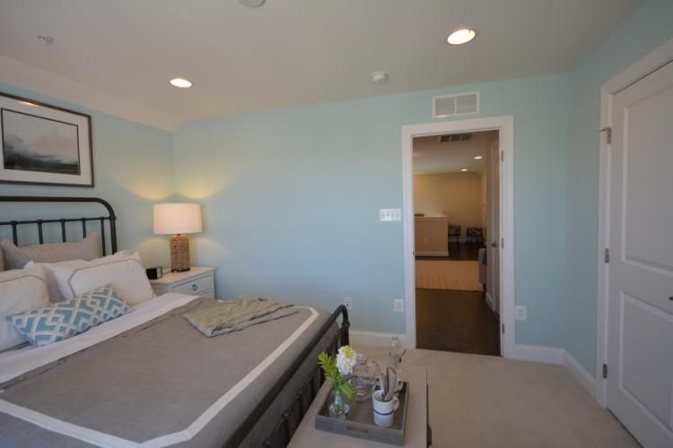Bedroom with light blue walls, gray bed, and door to another room.