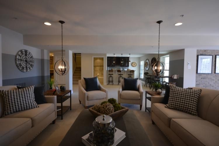 Living room with neutral sofas, armchairs, and pendant lights. Open concept with dining area visible in the background.
