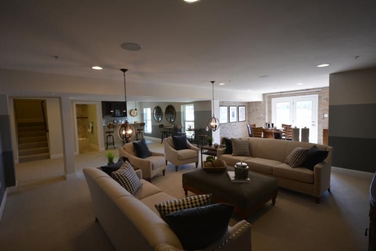 Spacious living room with sofas, armchairs, and a large ottoman. Neutral colors, recessed lighting, and access to other rooms.