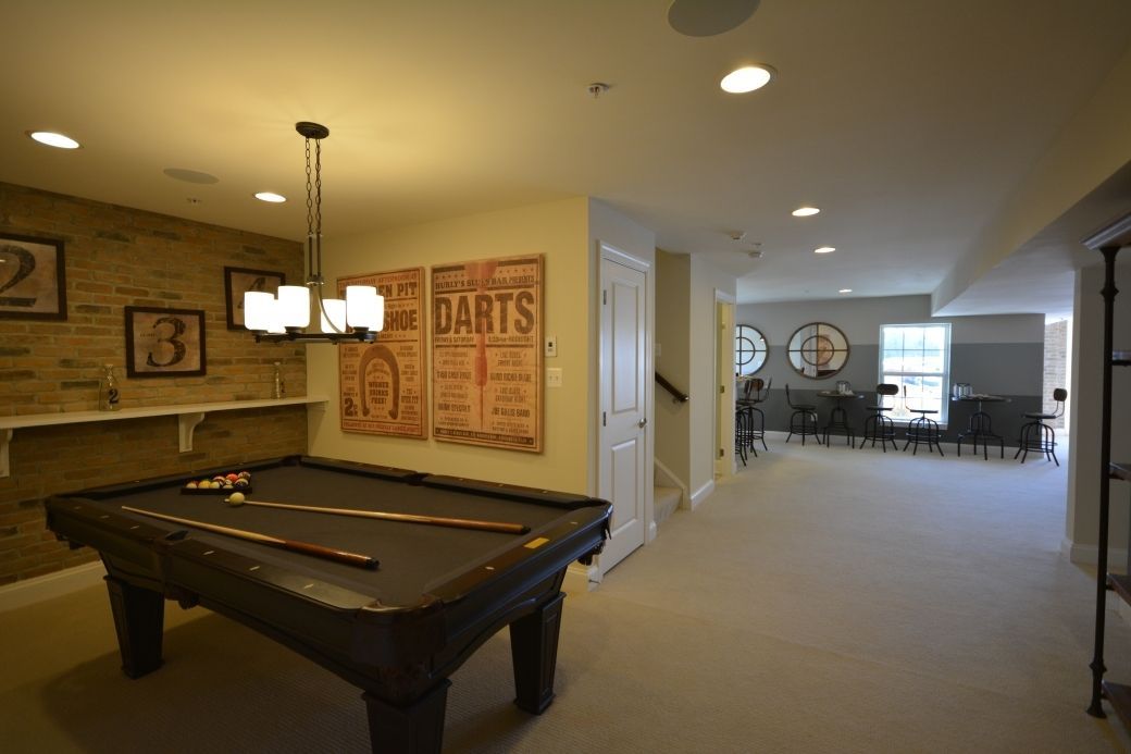 Pool table in a finished basement, with dart board art and a seating area.