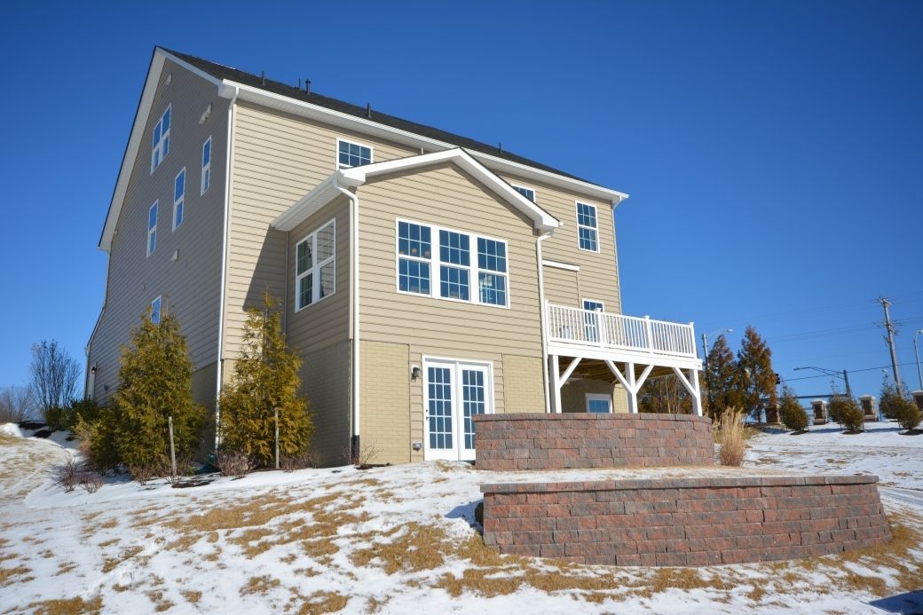 Two-story house with beige siding, white trim, and a deck. Snow on the ground, blue sky.