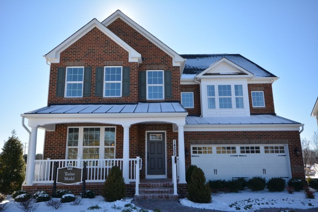 Brick house with snow, blue sky. Porch, shutters, garage, and architectural details.