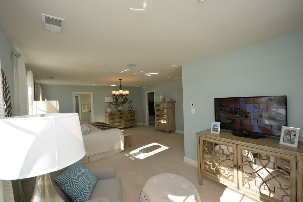 Bedroom with light blue walls, tan carpet, TV on a light brown cabinet.
