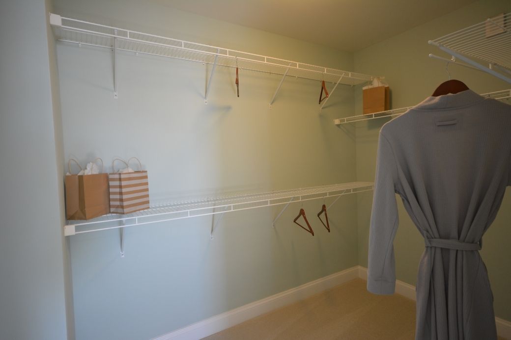 Empty walk-in closet with wire shelving and a hanging gray robe. Pale green walls and beige carpet.