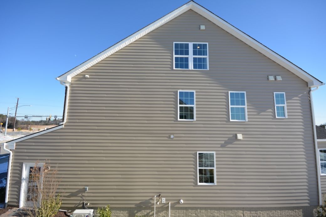 Tan siding on a two-story house with several windows against a clear blue sky.