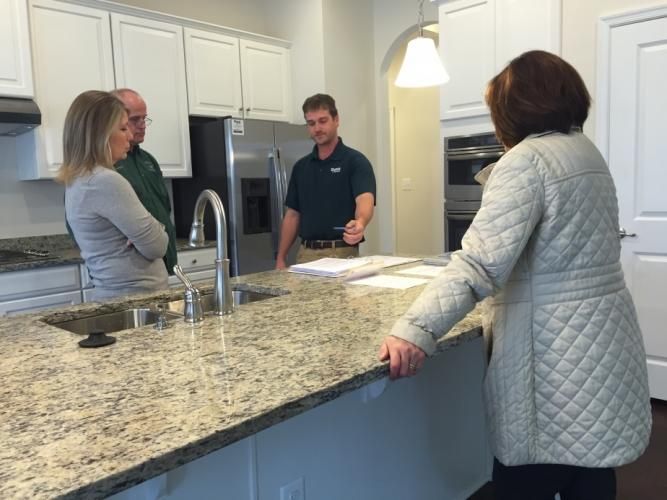 People in a kitchen viewing a countertop, discussing a design plan with a contractor.