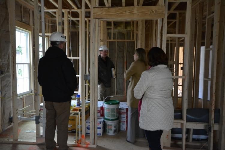 People in a framed home under construction, looking at the interior.