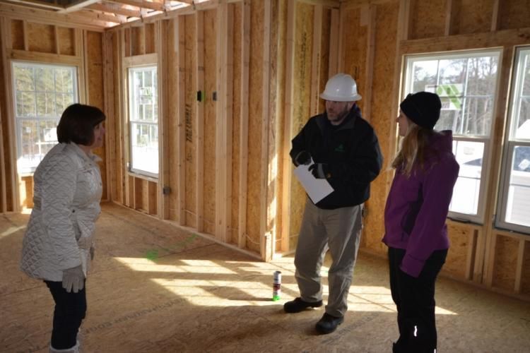 Inside a building under construction, a man in a hard hat speaks to two women.