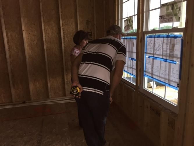 Man holding child, looking out window in unfinished house.