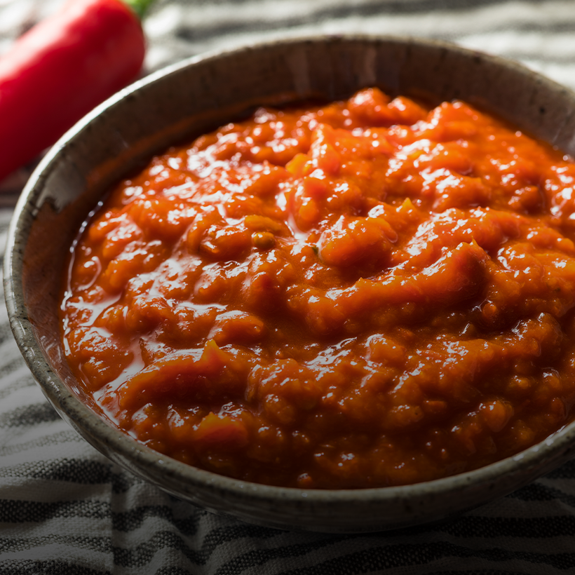 A close-up photograph of a vibrant red sambal paste, showcasing its rich color and texture